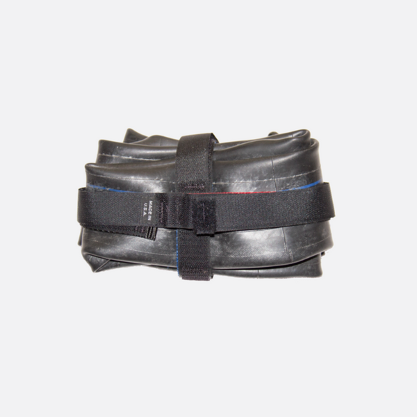 Deflated rubber tyre folded, wrapped with 2 black velcro straps. One strap vertical and one strap horizontal.