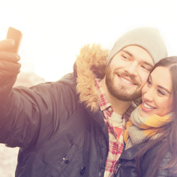 Couple taking selfie with touchscreen smartphone while wearing gloves with GloveTacts connectivity stickers.